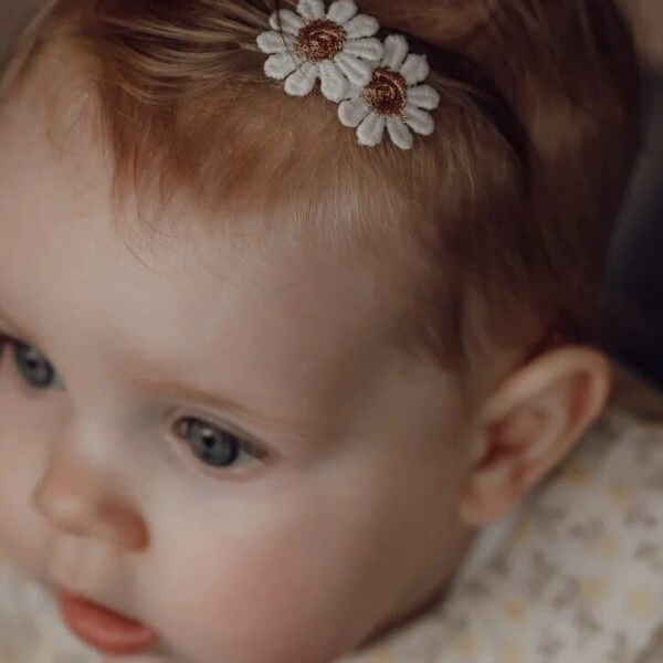 Een baby met fijn haar draagt een Daisy antislip haarspeldje met twee geborduurde madeliefjes. Het speldje houdt een los plukje haar opzij en blijft stevig zitten dankzij de antislip grip, perfect als eerste haarspeldje.