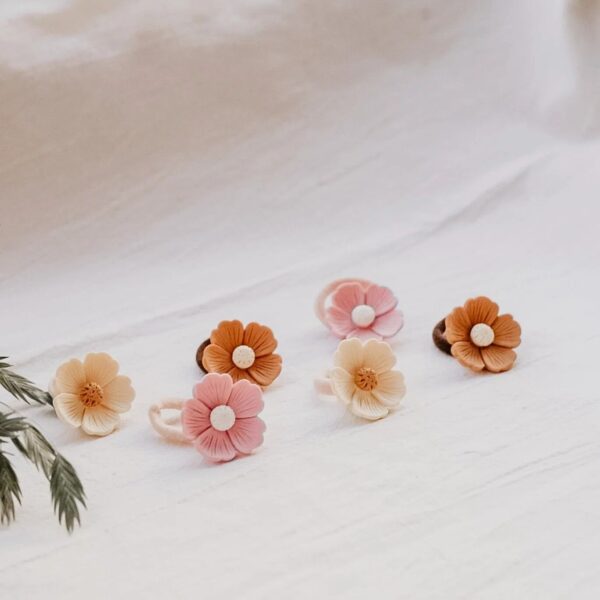 Zes elastiekjes met gedetailleerde bloemen in drie verschillende kleuren β crΓ¨me, oudroze en warm bruin β liggen op een lichte, zachte ondergrond. De neutrale tinten en subtiele details geven een natuurlijke en speelse uitstraling.