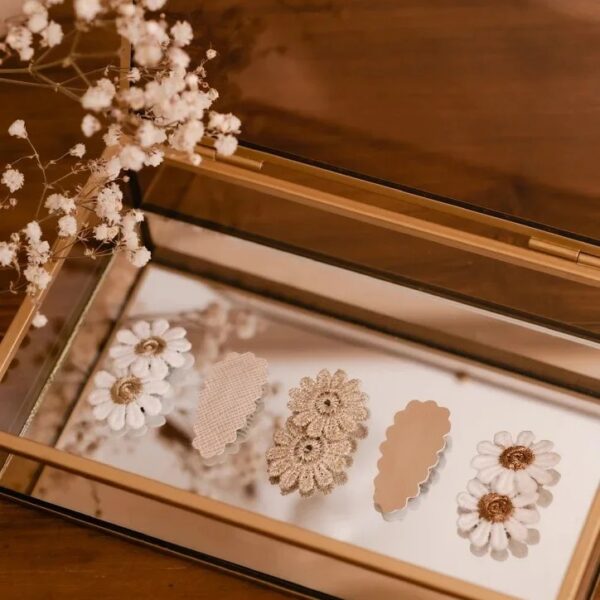 Een set van vier geborduurde en neutrale haarspeldjes ligt op een spiegelend sieradendoosje. De Senna set bevat antislip speldjes met bloemen en zachte tinten, perfect voor fijne kinderhaartjes.
