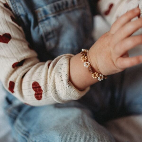 Kinderarmbandje met bloemen van kralen in zachte lente kleuren, gemaakt met Miyuki kralen en gedragen om de pols van een kindje.