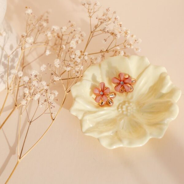 Twee perzikroze bloemvormige haarklemmetjes met glinsterende steen in het midden, gepresenteerd op een lichtgele bloemenkom met droogbloemen ernaast.