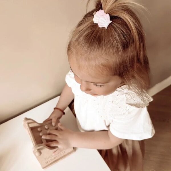 Blij meisje speelt met een houten kassa, draagt een glitterend schelpjespeldje van Little Yune in haar haar.