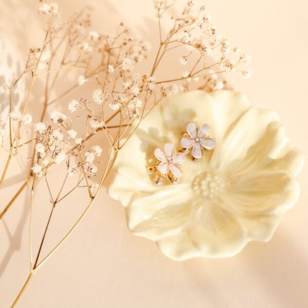 Twee witte bloemetjes-haarklemmetjes met glinsterende details, gepresenteerd op een crèmekleurig bloemen schaaltje met droogbloemen.