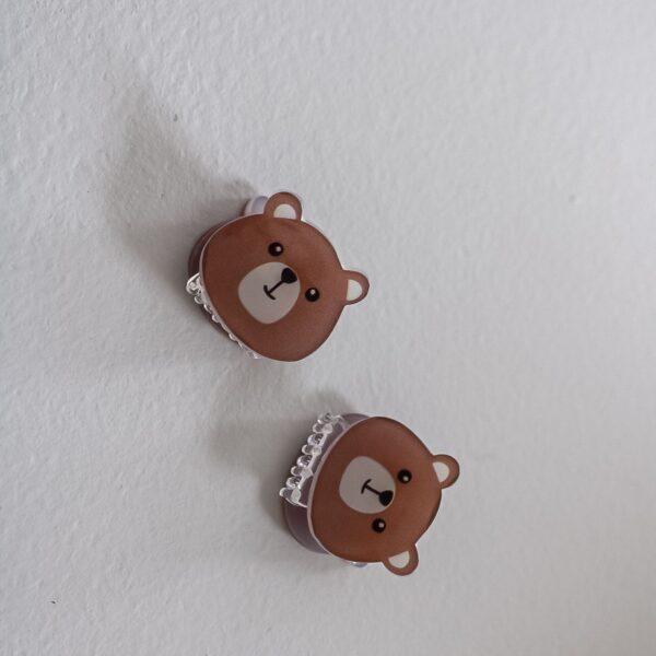 Twee bruine teddy haarklemmetjes met schattig beertjesgezichtje op een witte achtergrond, met transparante tandjes.