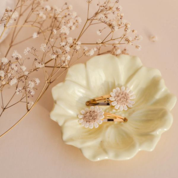 Twee klikklakspeldjes met madeliefjesdesign in een sierlijk bloemenschaaltje, perfect voor schattige hair-do's en twinning momentjes.