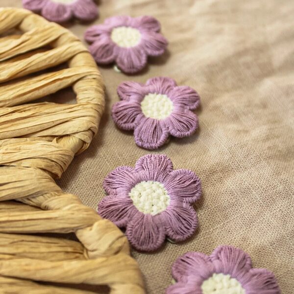 Zes paarse bloemvormige antislip haarspeldjes "Ninte" met een crèmekleurig hartje, liggend op een beige linnen doek naast een gevlochten naturel rieten accessoire. Perfect als los speldje of als onderdeel van set Sara. 🌸💜