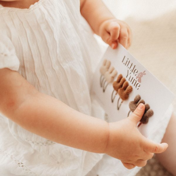 Peuterhandjes houden een Little Yune kaart met zes bunny klikklak haarspeldjes van 3 cm in neutrale tinten.