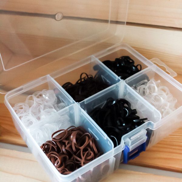 Doorzichtige bewaardoos gevuld met 2500 neutrale haarelastiekjes in zwart, bruin, wit en transparant.