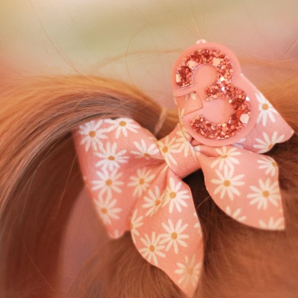 Kinderhaar in staartje met roze verjaardagsstrik met witte bloemetjes en glittercijfer 3.