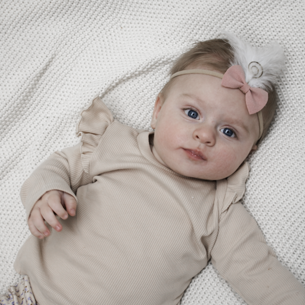 Baby met roze haarbandje en gouden veertje, in een herfstoutfit zittend op bed met sinterklaasdecoratie.
