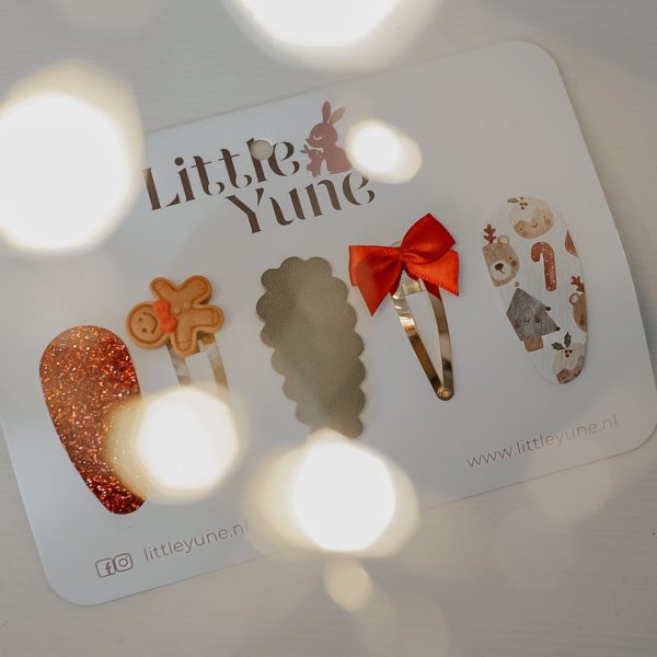 Klein meisje met glanzende roze haarband bekijkt een kaartje met vijf Little Yune haarspeldjes uit Setje Ginger – kerst haarspeldjes met glitter, rood strikje en peperkoekthema (verkrijgbaar in 3, 4 en 5 cm).