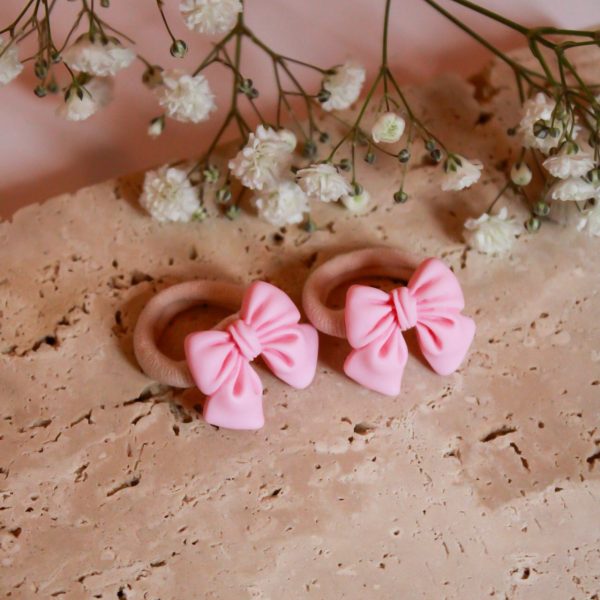 Twee lichtroze strik-elastiekjes op beige steen met witte bloemetjes erboven, in zachte Little Yune-stijl.