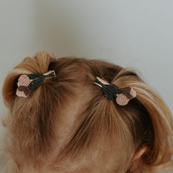 Twee kleine alligator haarspeldjes met donkergroene strikjes en zachte pompom-details, gedragen in twee staartjes bij een meisje.