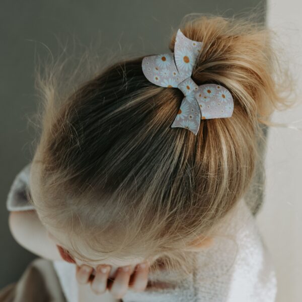 Statement strik in een nieuwe vorm met madeliefjesprint, bevestigd op een 4 cm alligator haarspeldje en gedragen in een staart bij een meisje.