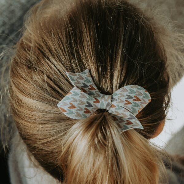 Statement strik in een nieuwe vorm met pastel hartjesprint, bevestigd op een 4 cm alligator haarspeldje en gedragen in een lage staart.