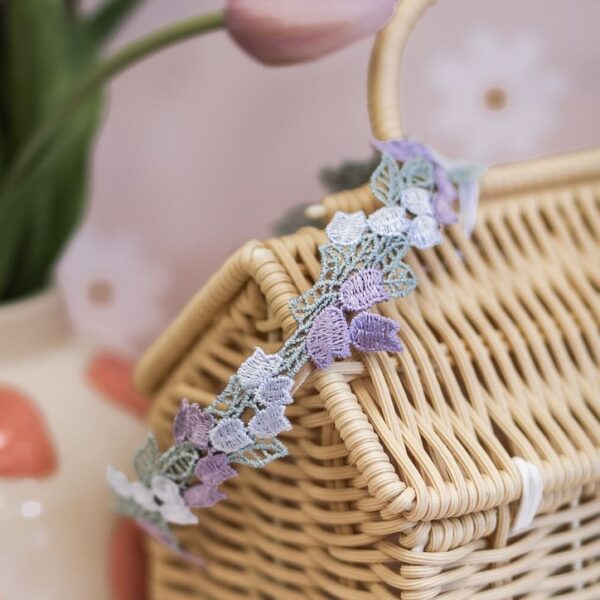 Pastel bloemen diadeem voor meisjes met lila en zachte blauwtinten, gedragen in blond haar en gefotografeerd in zachte natuurlijke setting.