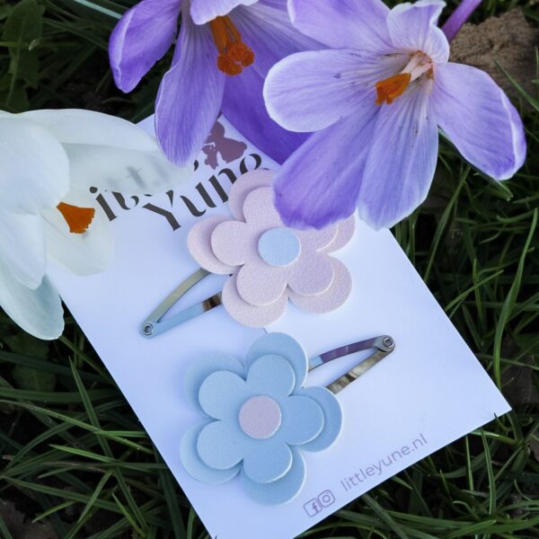 Twee madelief haarspeldjes in pastel roze en lichtblauw op 4 cm klikklakspeldjes van Little Yune, gestyled tussen paarse krokus bloemen in het gras.