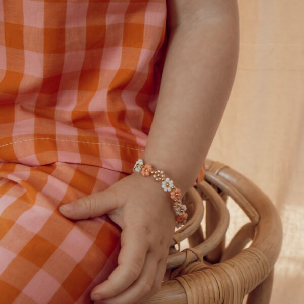 Peach Daisy armbandje voor meisjes met madeliefjes, peachkleurige kralen, witte bloemetjes en gouden details, verkrijgbaar in twee maten voor kleine en grotere meisjes.